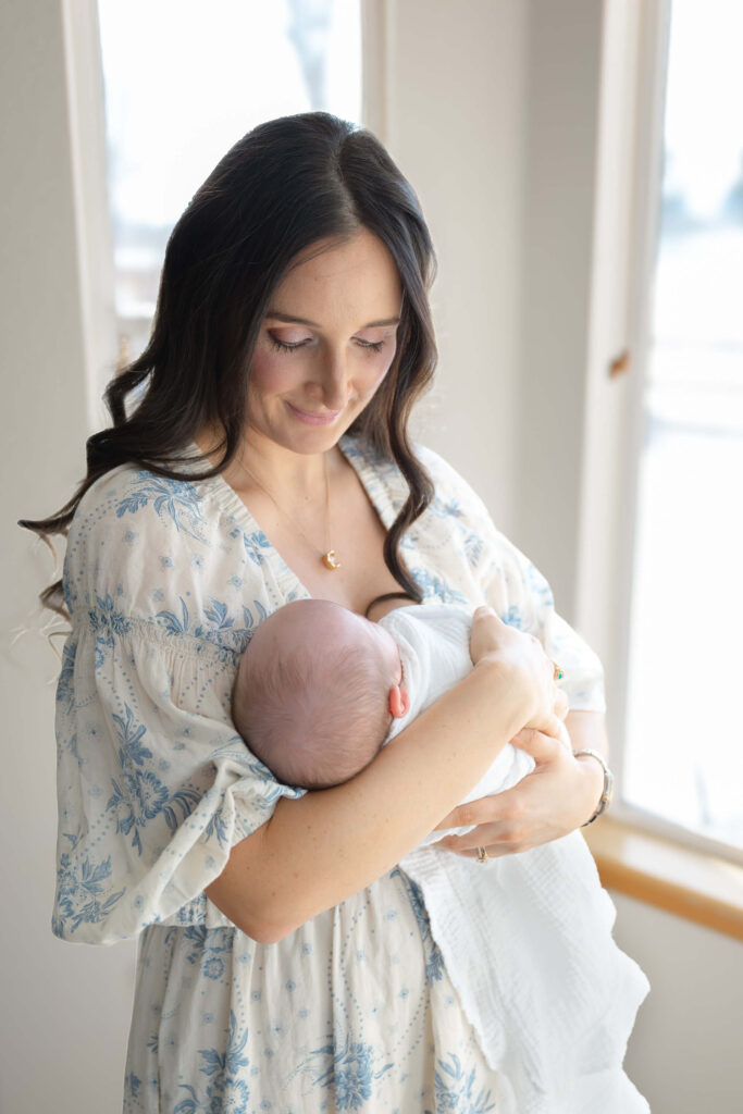 Mom holding newborn baby while looking out the window during a Fort Collins lifestyle session