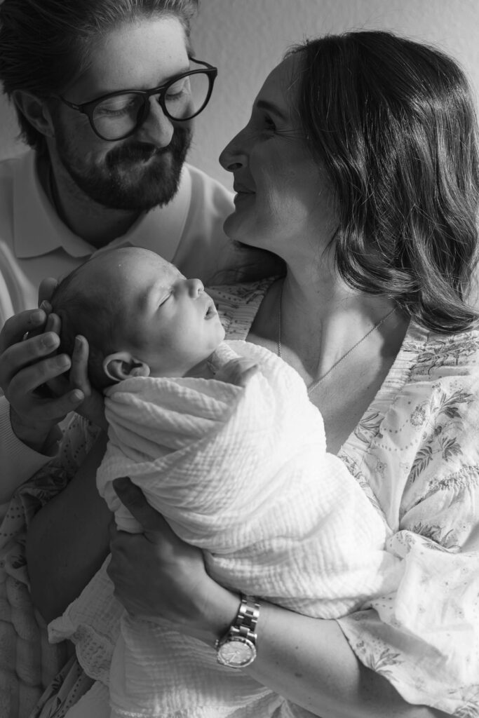 Mom and dad smiling at each other while holding their newborn during a Fort Collins in-home session