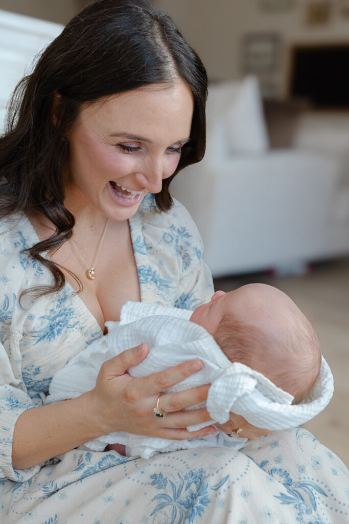 Mom sitting and laughing with her newborn baby during a Northern Colorado in-home session