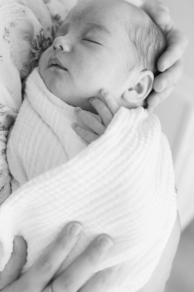 Black and white detail of newborn baby swaddled with dad's hand beside them during a Fort Collins in-home session